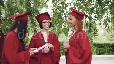 三位漂亮的女毕业生在毕业典礼上交谈并持有毕业证书，学生们感到骄傲和兴奋